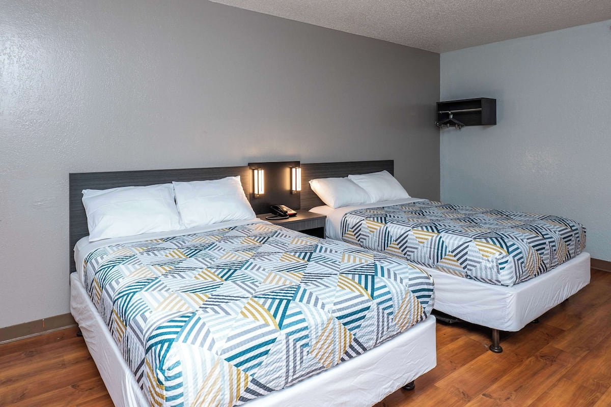 Une chambre d’hôtel avec deux lits, une table de chevet avec un téléphone et un luminaire fixé au mur.