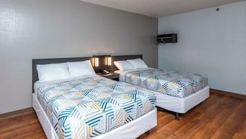 A hotel room with two beds, a bedside table with a phone, and a wall-mounted light fixture.