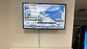 A modern hotel reception area with a large flat-screen TV displaying a weather forecast.