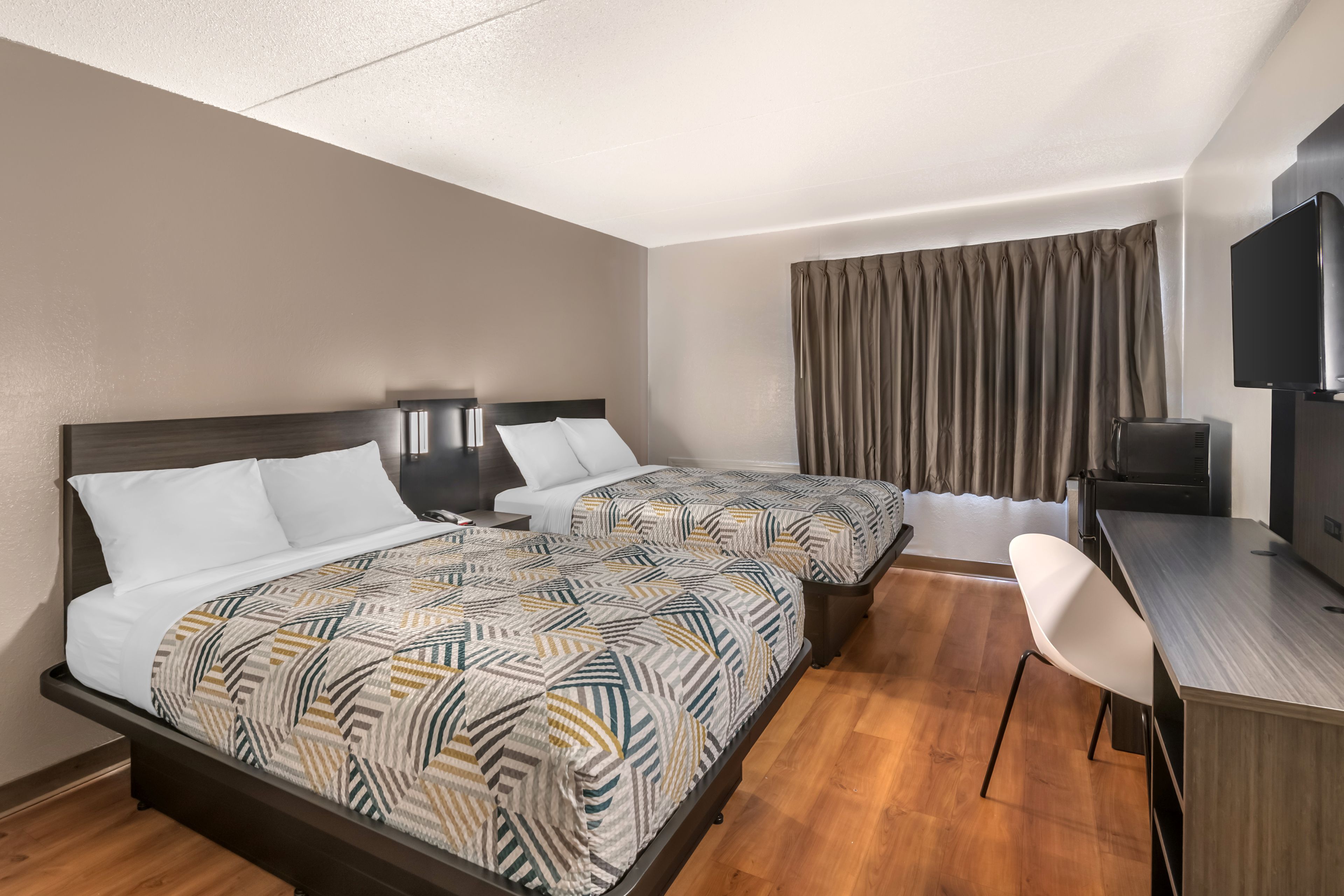 A hotel room with two beds, a desk, a chair, a television, and a window with curtains.