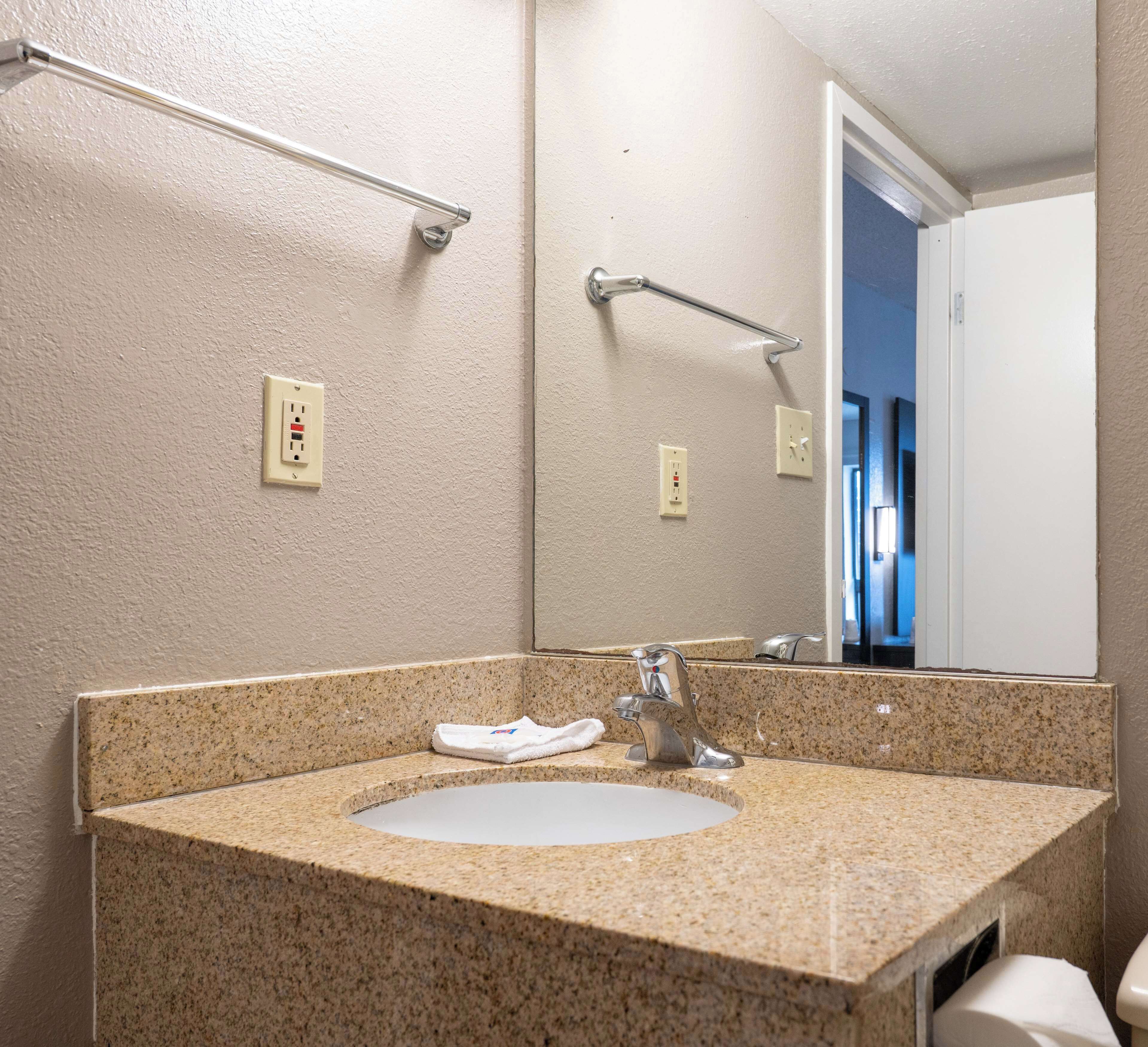 A bathroom with a granite countertop sink, a mirror, and a towel rack.