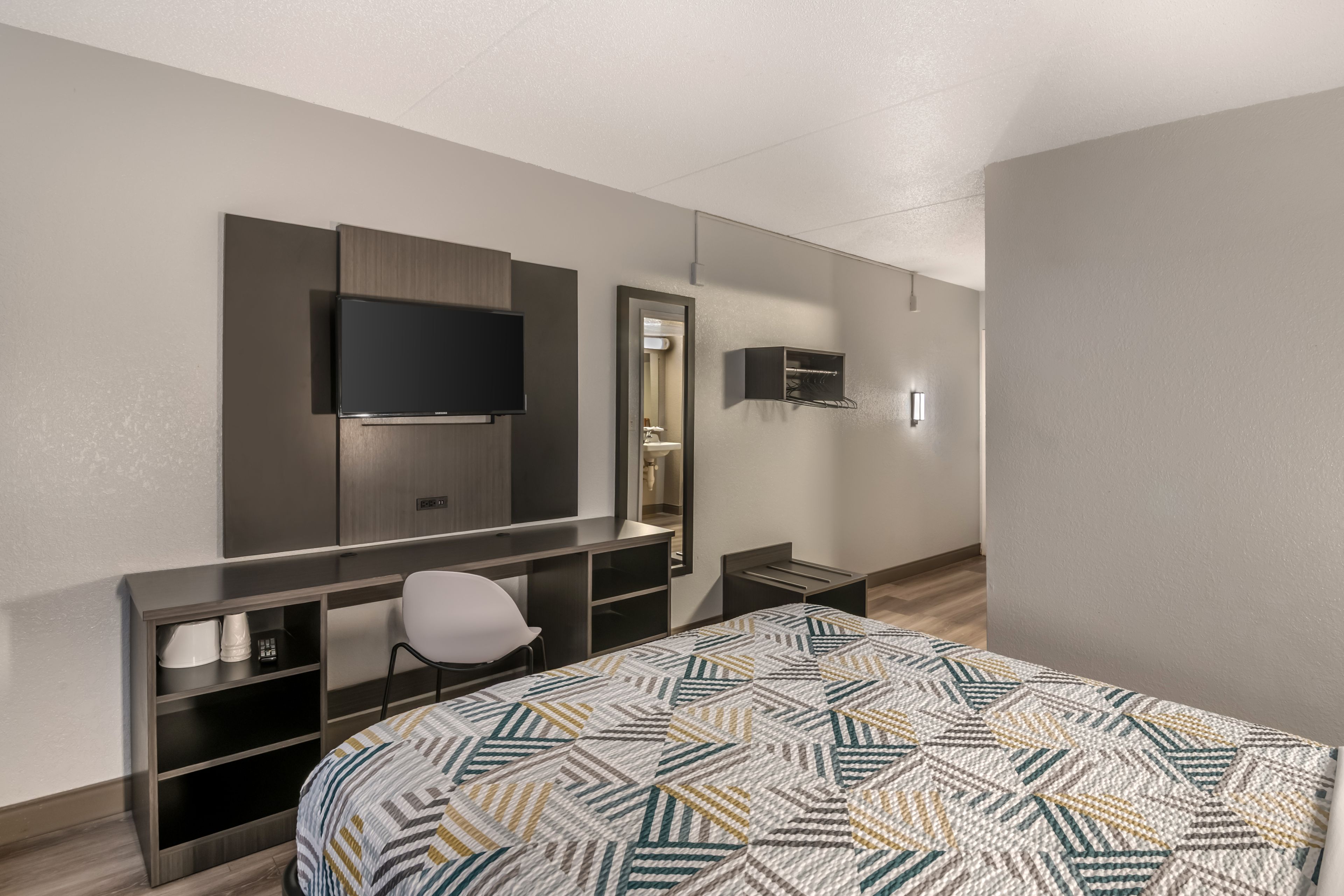 A hotel room with a bed, a desk, a chair, a television, and a mirror.