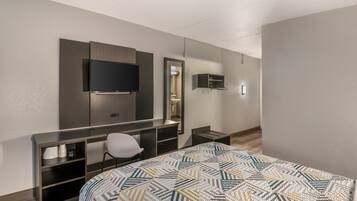 A hotel room with a bed, a desk, a chair, a television, and a mirror.