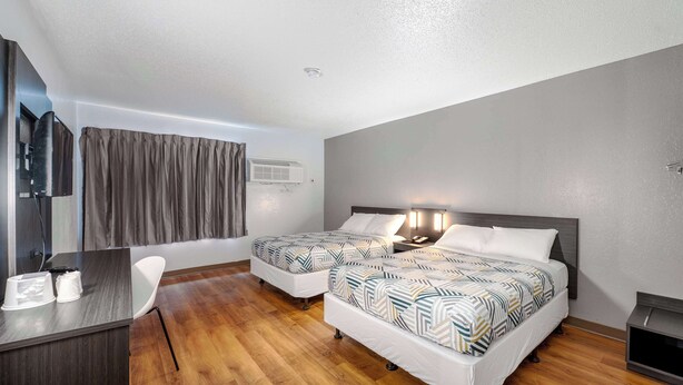 A hotel room with two beds, a desk, a chair, and an air conditioning unit on the wall.