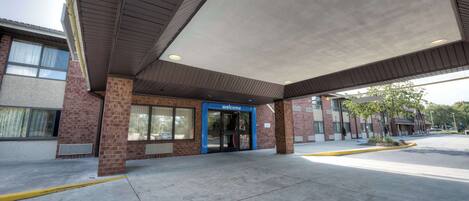 A building entrance with a 'welcome' sign, a covered area, and a clear sidewalk.
