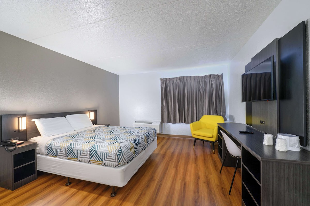 Une chambre d’hôtel moderne équipée d’un lit, d’un bureau, d’une chaise, d’une télévision et d’une fenêtre avec des rideaux.