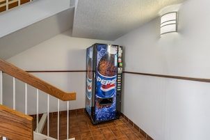 Una máquina expendedora con el logo de Pepsi, ubicada en un pasillo con una escalera de madera.