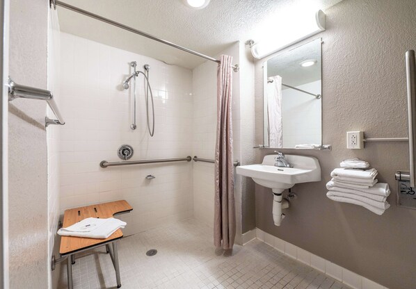 Un baño con ducha, lavamanos, espejo y toallero.