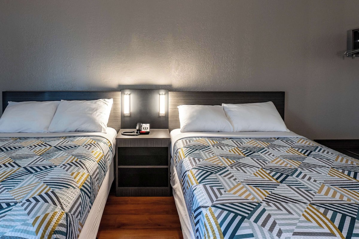 Une chambre d’hôtel avec deux lits, chacun agrémenté de draps à motifs, une table de chevet avec un téléphone et un luminaire fixé au mur.