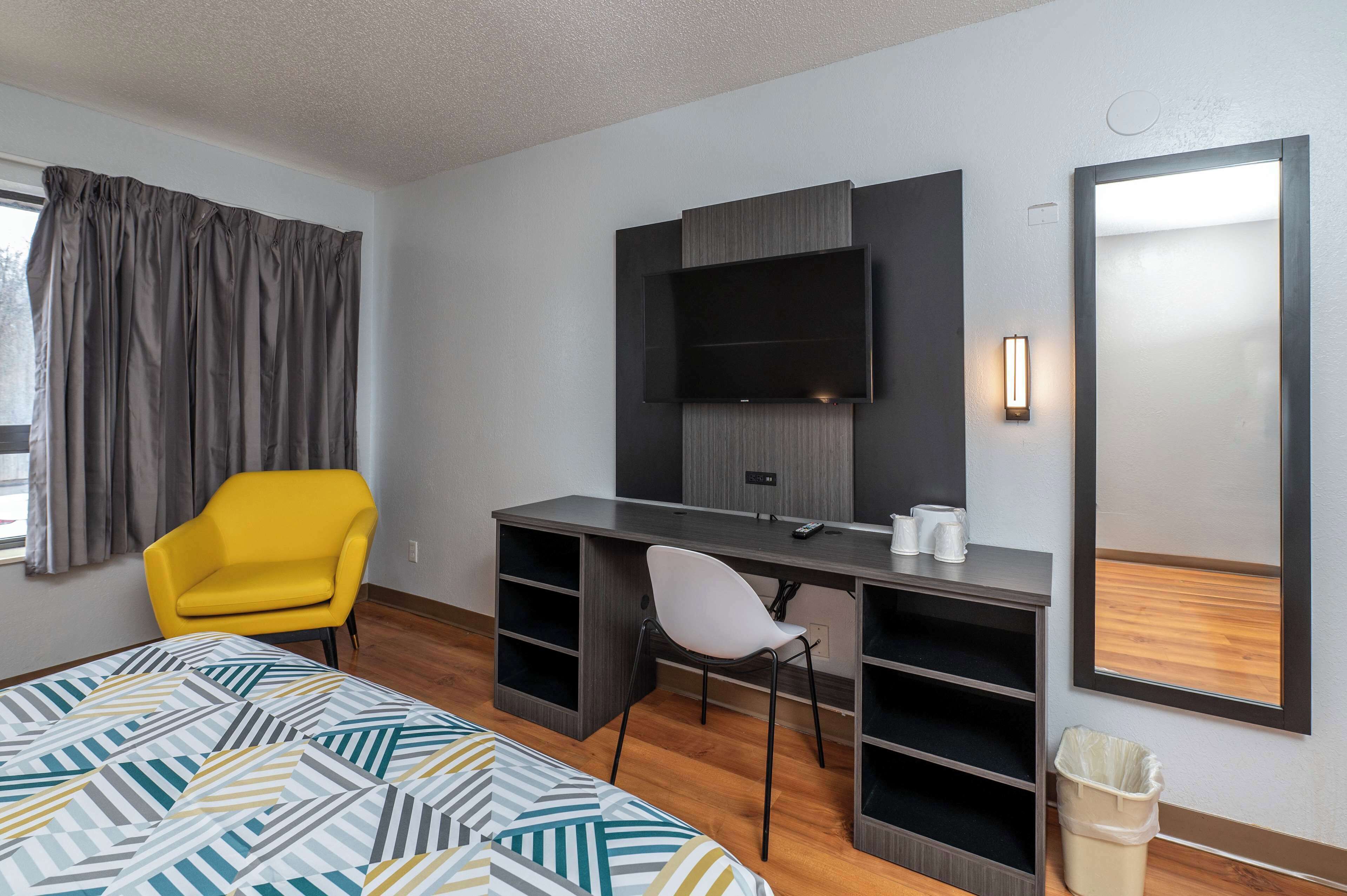 A hotel room with a bed, a desk with a chair, a TV, and a mirror.