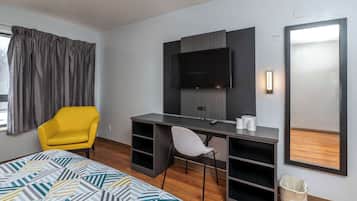 A hotel room with a bed, a desk with a chair, a TV, and a mirror.