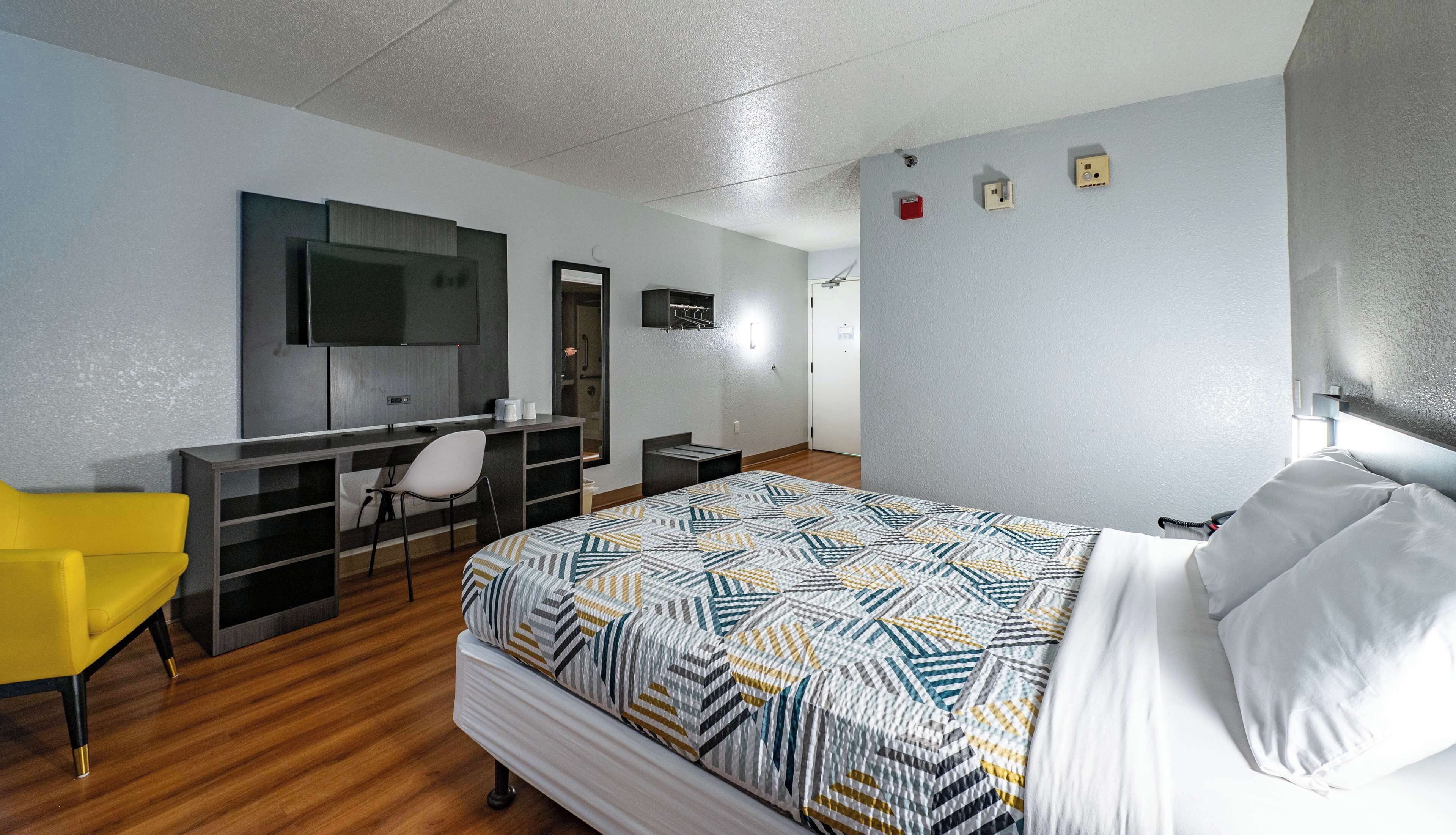 A hotel room with a bed, a desk with a chair, a television, and a wardrobe.