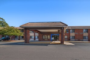Un motel con área de estacionamiento techada, fachada de ladrillo y un letrero de 'Welcome'.