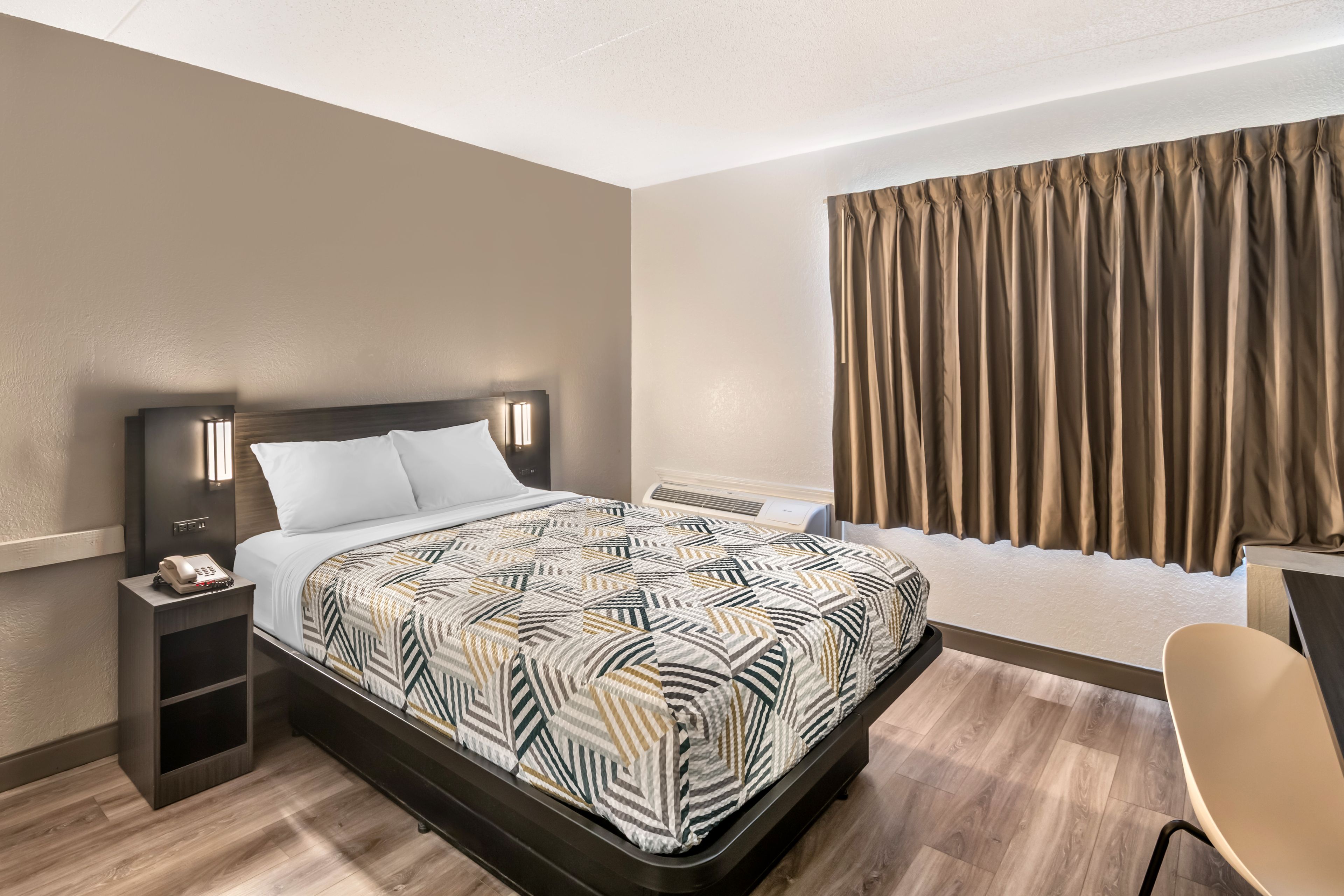 Ein Hotelzimmer mit Bett, Nachttisch, Stuhl und Vorhängen.