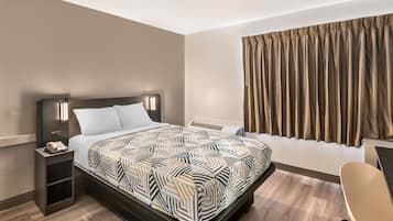 Ein Hotelzimmer mit Bett, Nachttisch, Stuhl und Vorhängen.