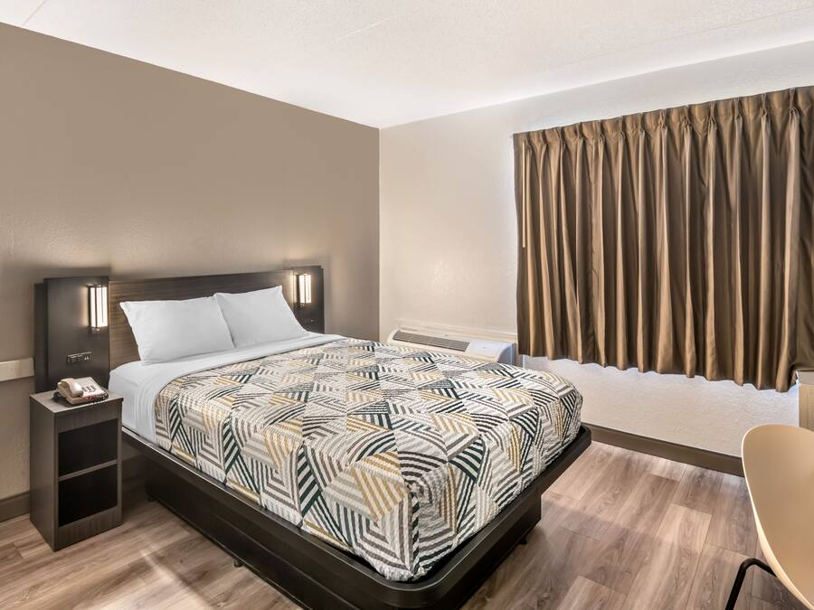 Ein Hotelzimmer mit Bett, Nachttisch, Stuhl und Vorhängen.