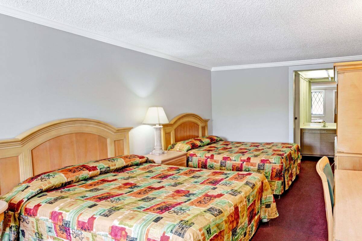 A hotel room with two beds, a nightstand, a lamp, and a wooden wardrobe.
