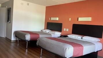 A hotel room with two beds, a wooden floor, and a plain wall with a thermostat.