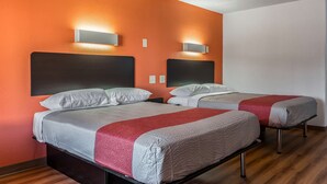 A hotel room with two beds, orange walls, and modern wall sconces. - Motel 6 White, GA - Cartersville (White)