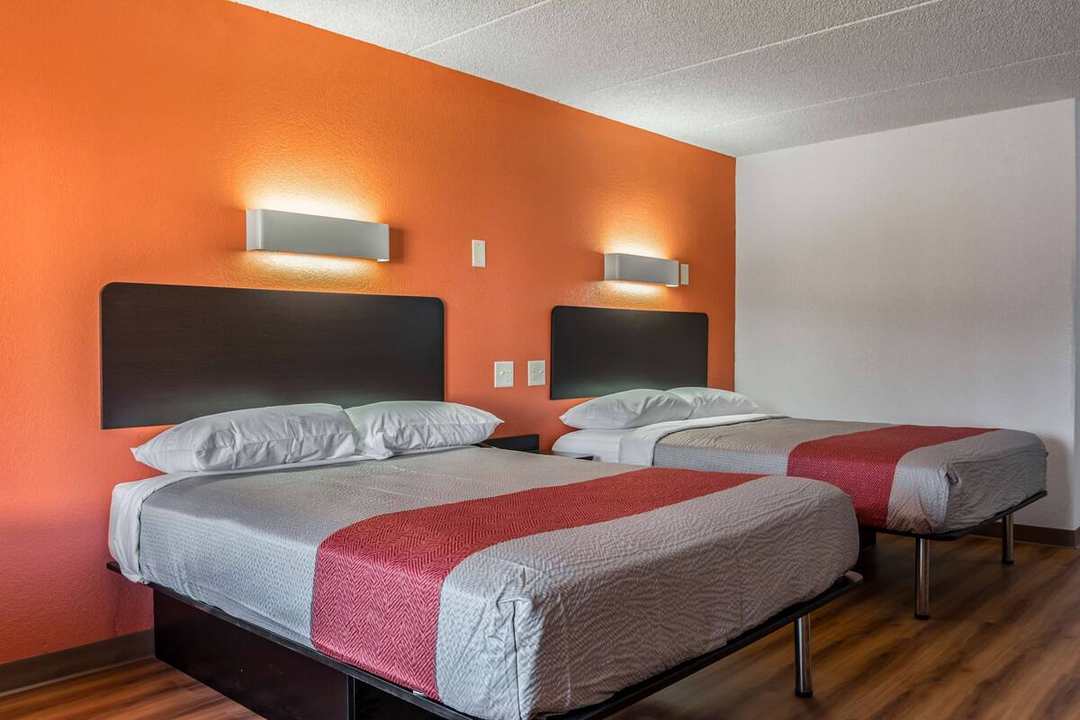Ein Hotelzimmer mit zwei Betten, orangen Wänden und modernen Wandleuchten.