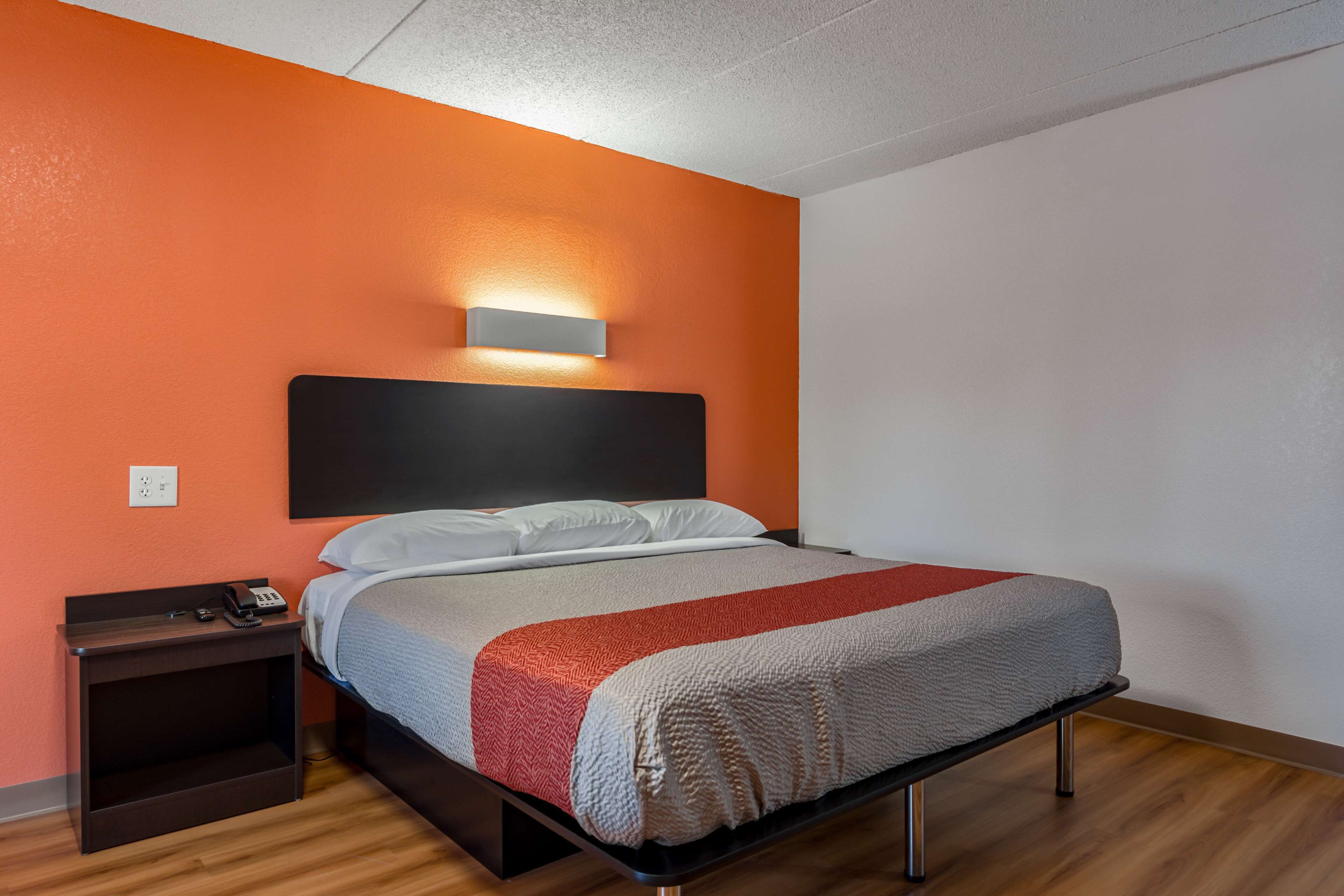 A modern hotel room with a bed, a nightstand, and a wall-mounted light.