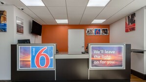 A hotel reception area with a modern design, featuring a reception desk, a large illuminated sign, and a door leading to the rooms. - Motel 6 White, GA - Cartersville (White)