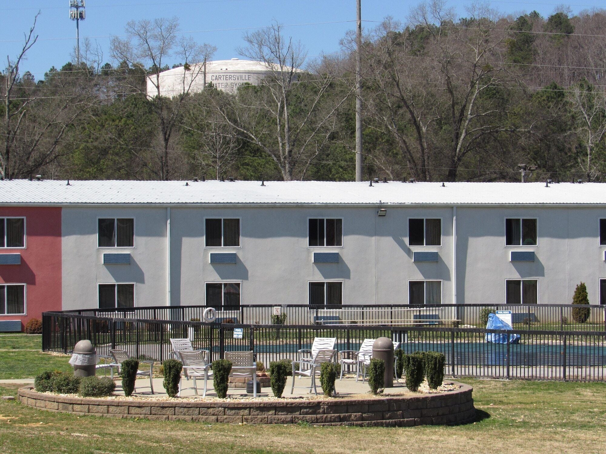 A building with multiple windows and a fenced outdoor area with chairs and small trees.