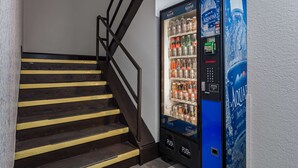 A staircase with black railings and yellow stripes, next to a blue vending machine stocked with beverages. - Motel 6 White, GA - Cartersville (White)