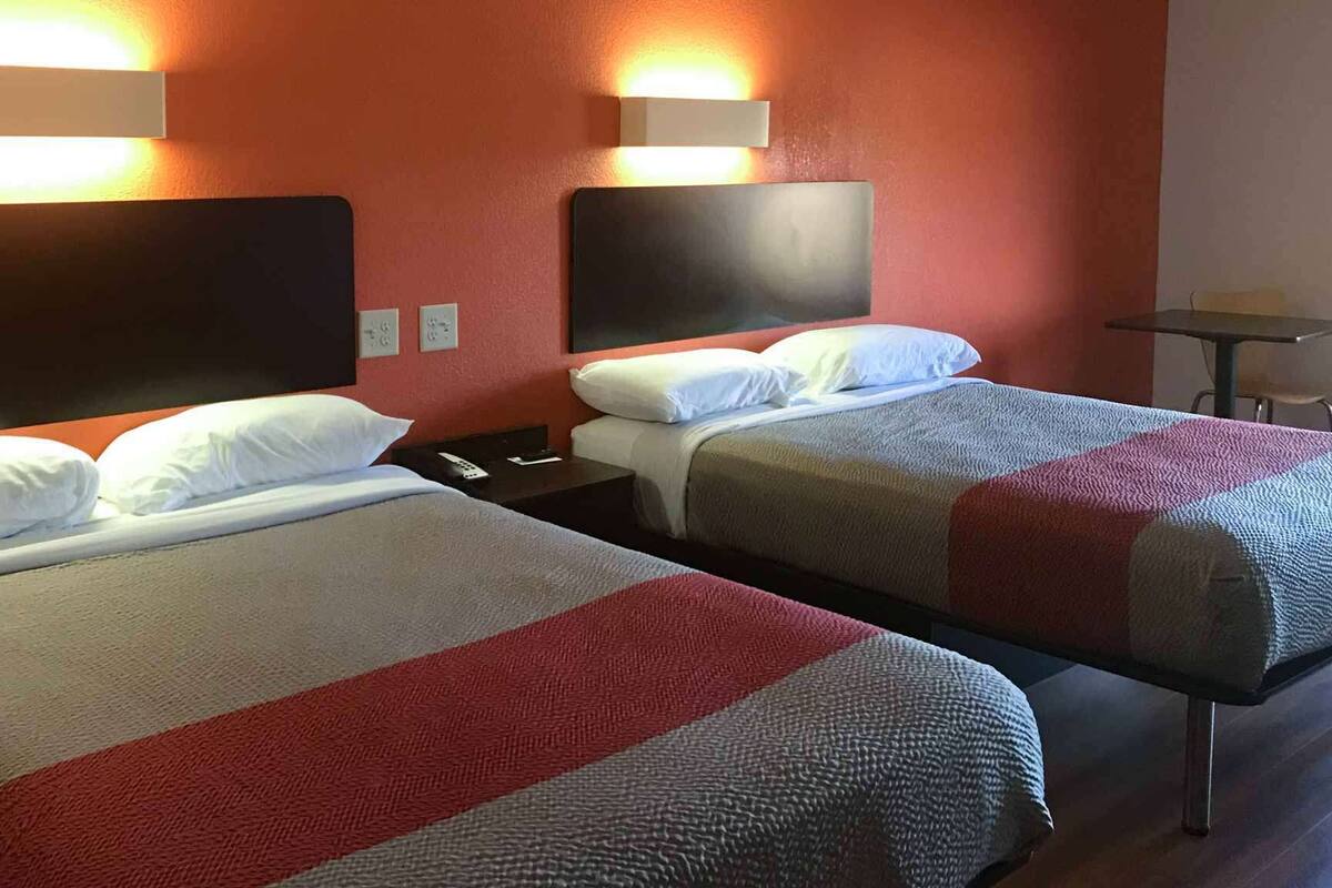 Zwei Einzelbetten mit Kopfteilen, ein kleiner Tisch und ein Stuhl in einem Zimmer mit roten Wänden und zwei Wandleuchten.