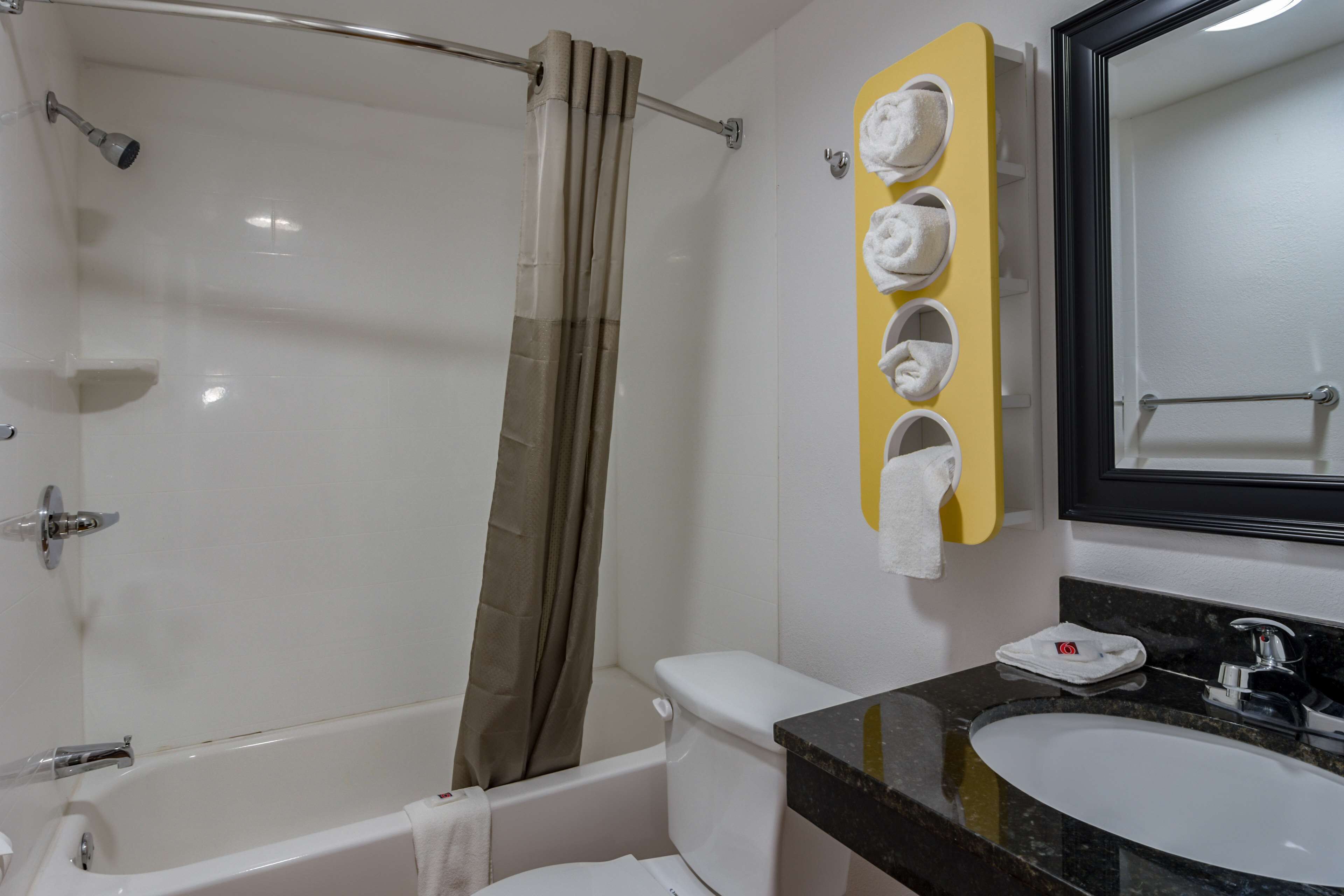 A bathroom with a bathtub, toilet, and sink. There is a shower curtain, a towel rack with towels, and a mirror above the sink.