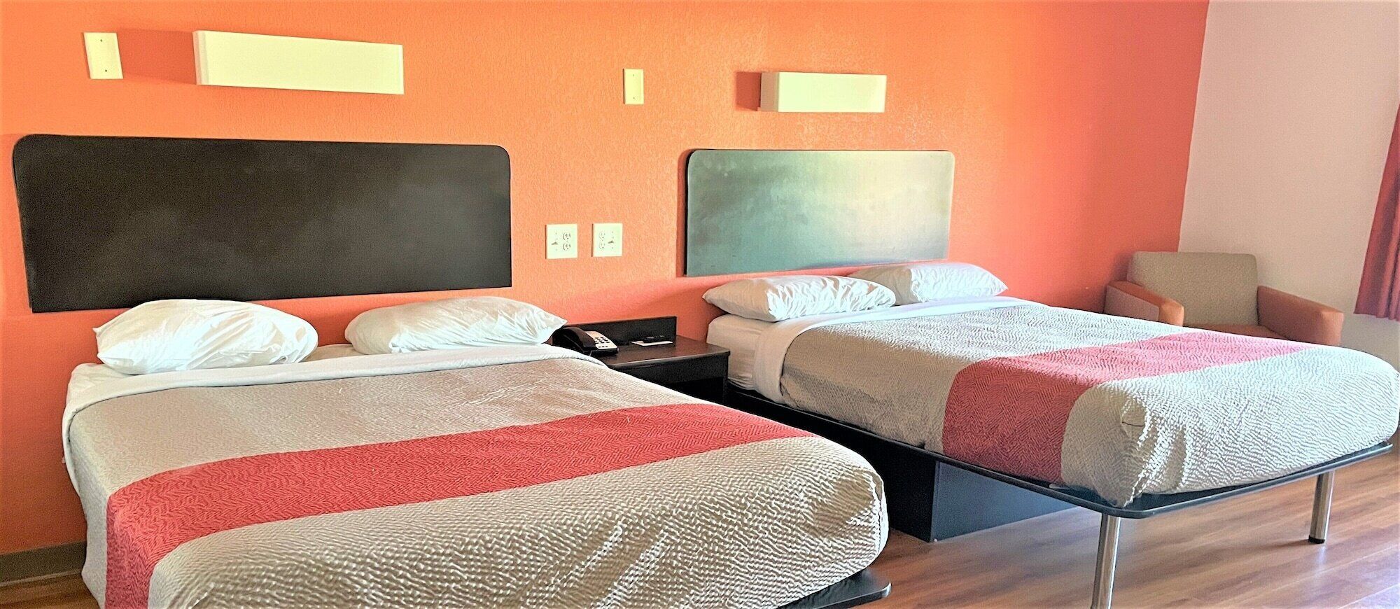 A hotel room with two beds, each with a headboard, a nightstand, and a chair.