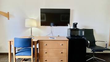 A hotel room with a desk, chair, TV, and a coffee maker.