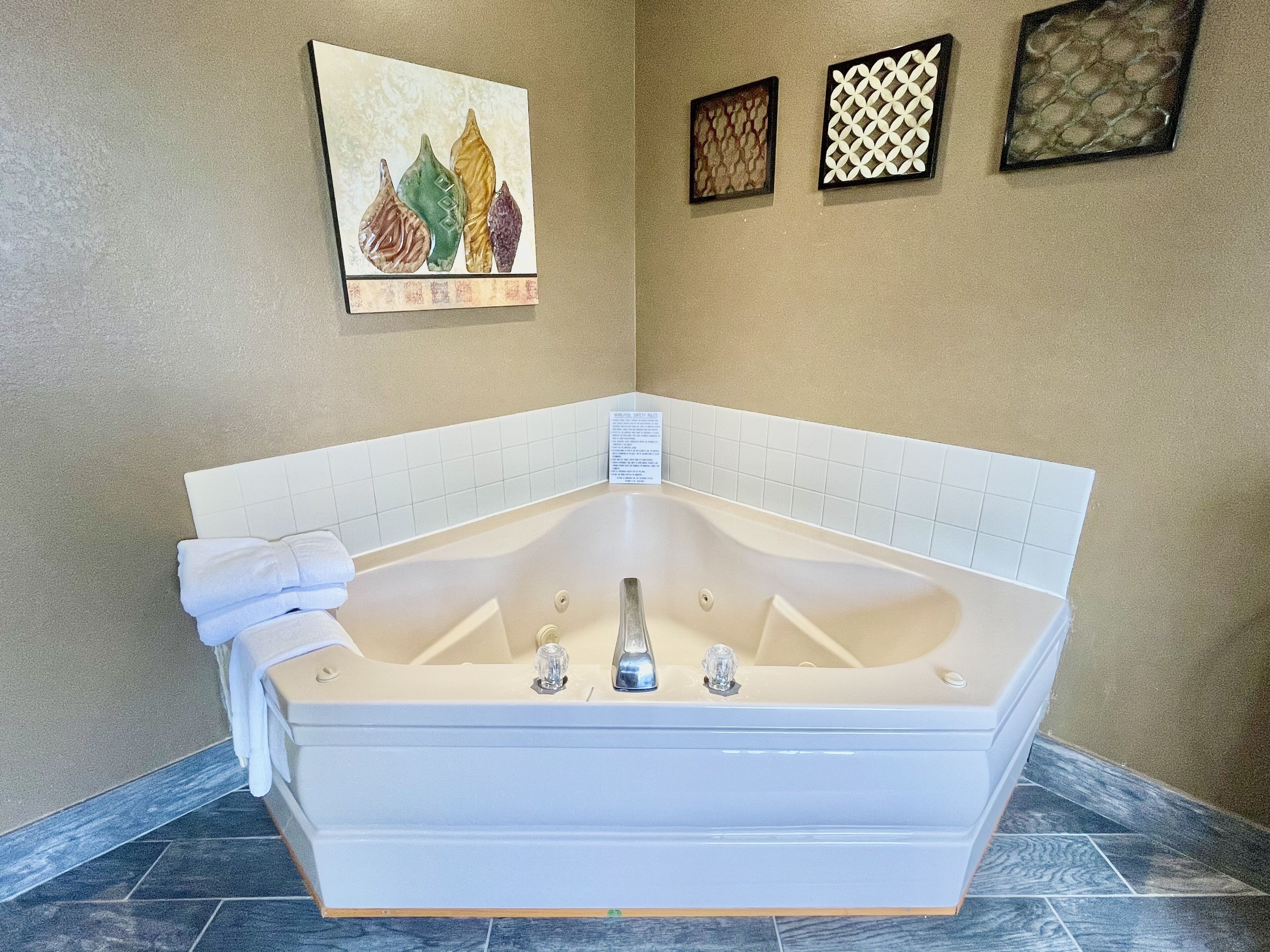 A corner bathroom with a freestanding bathtub, a towel, and three framed artworks on the wall.