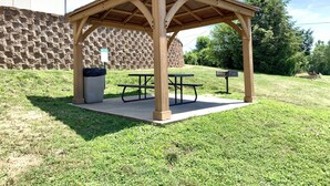 Un porxo de fusta amb taules de picnic i un cubell d'escombraries.