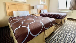 Habitació d'hotel amb dos llits, un capçaleri, una tauleta de nit, una làmpada i una finestra amb cortines.