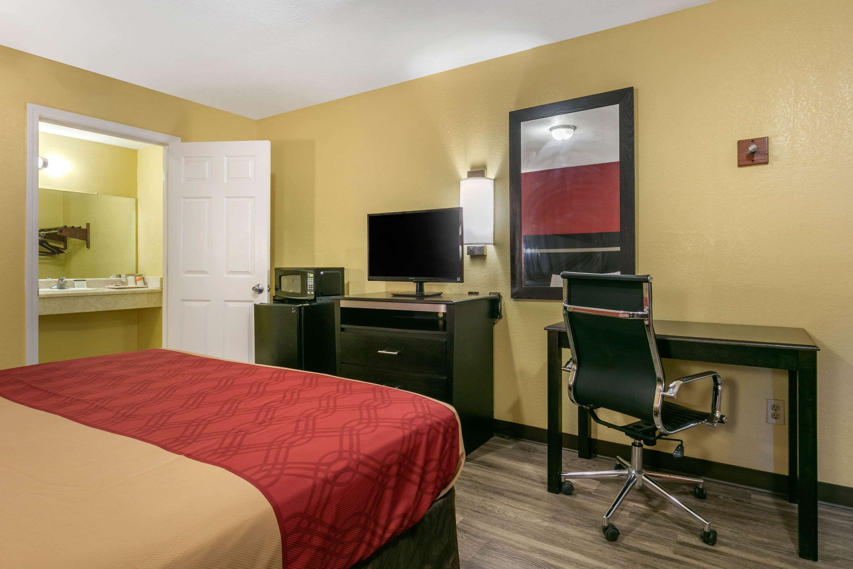 A hotel room with a bed, a desk with a computer, a TV, and a mirror.