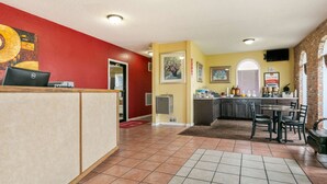 A hotel lobby with a reception desk, a kitchen area, and a dining space.