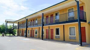A two-story motel with a yellow facade, multiple rooms with red doors, and a covered parking area.