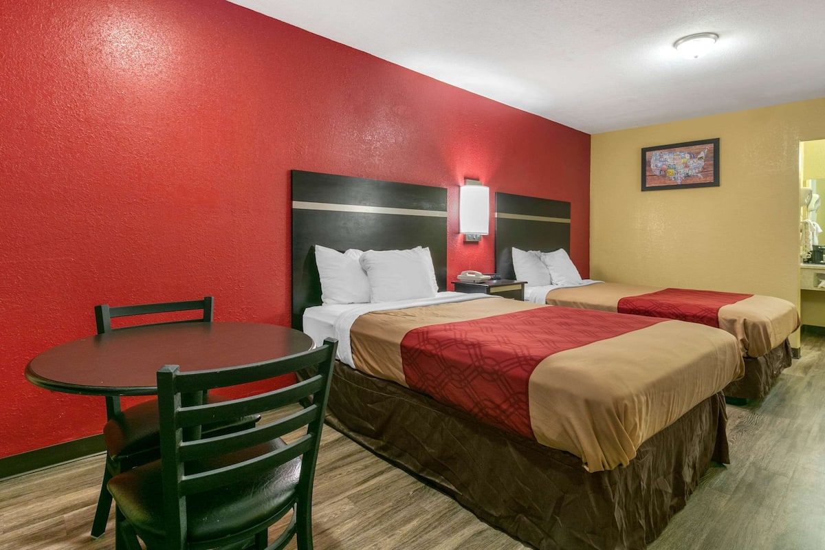 A hotel room with two beds, a small table, and a chair.