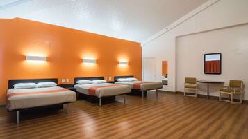 Une chambre d’hôtel avec trois lits, une petite table, deux chaises et un tableau au mur.