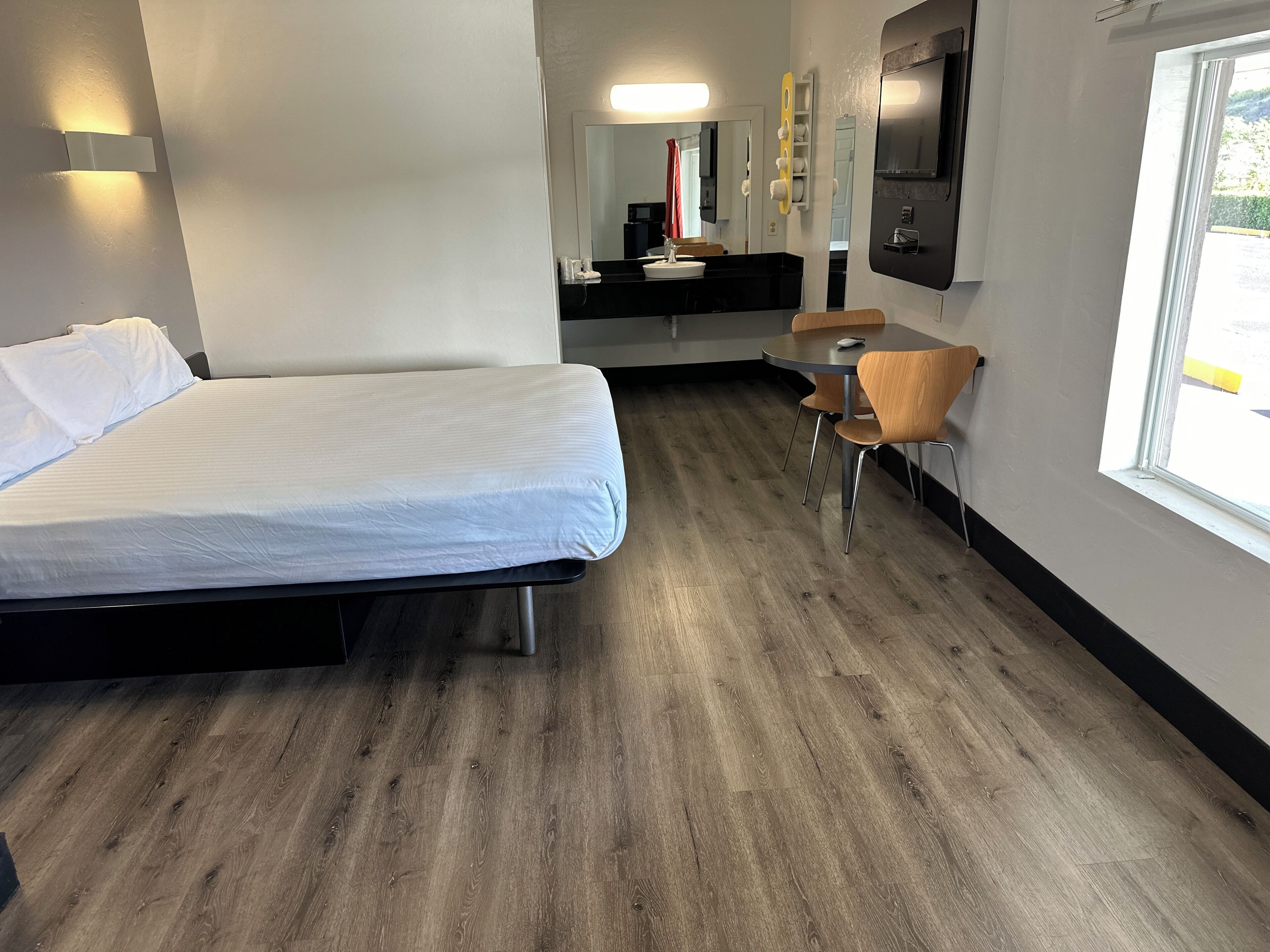 Habitació d'hotel amb llit, una petita taula i cadires, un lavabo i un mirall.