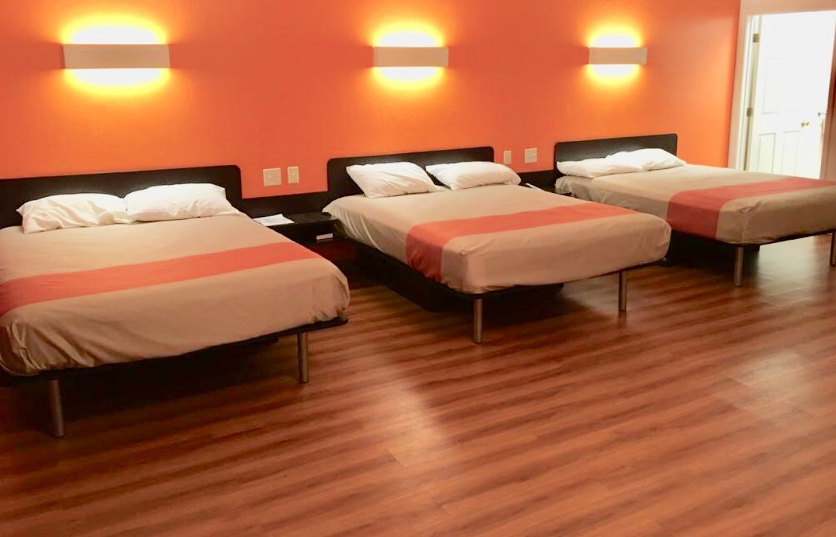 A hotel room with three beds, each with a wooden headboard and a white bedspread.