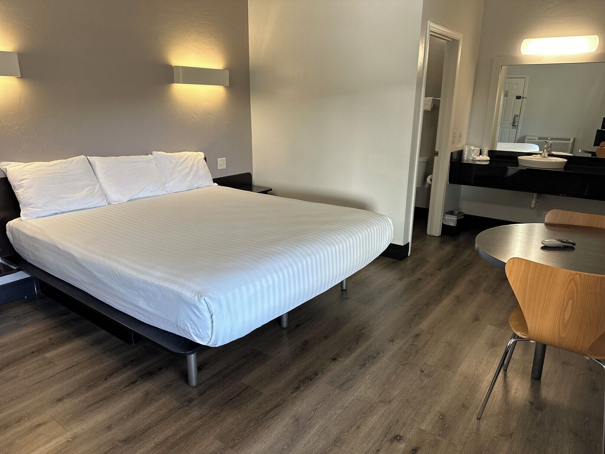 A hotel room with a bed, bedside table, and a small round table with a chair.