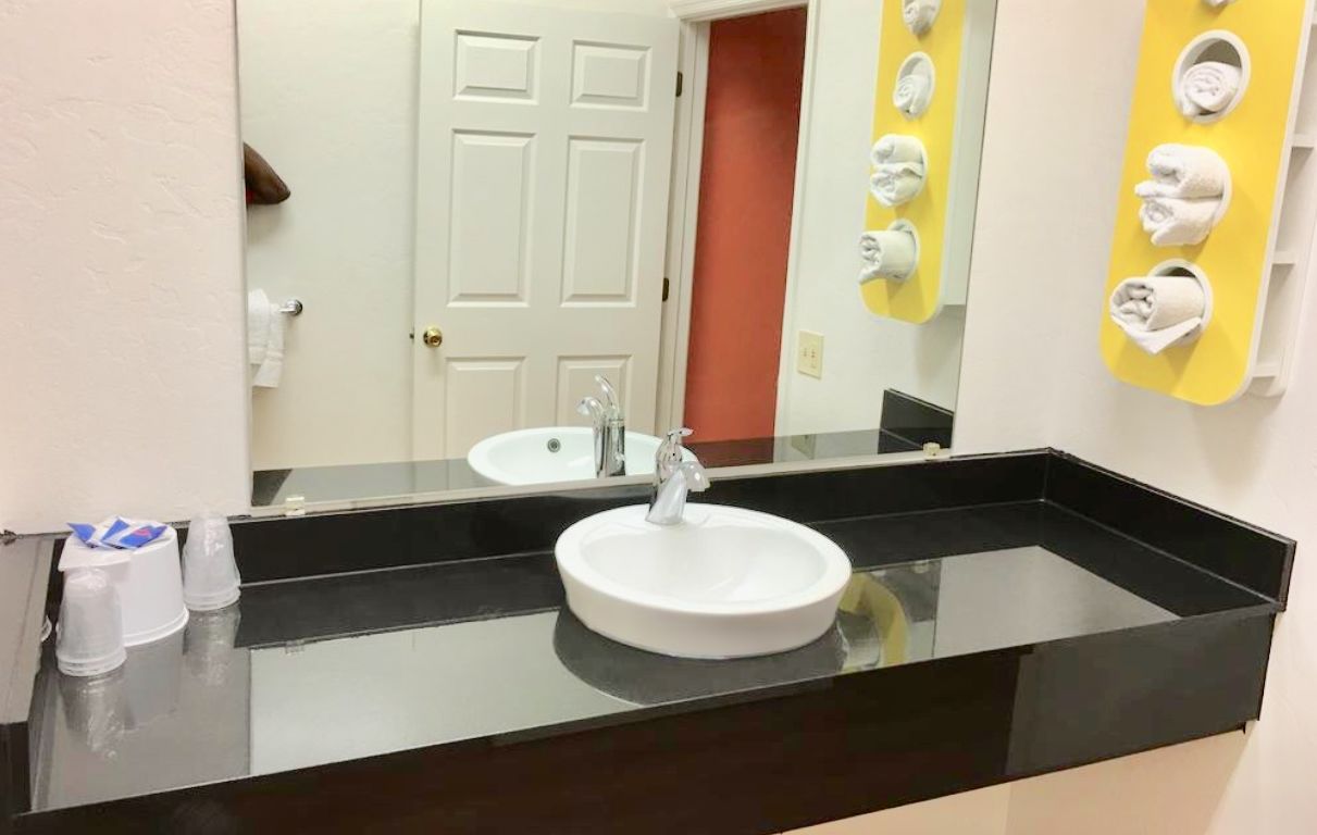 A bathroom with a white sink, black countertop, and a mirror. There are towels hanging on a yellow rack and a door in the background.