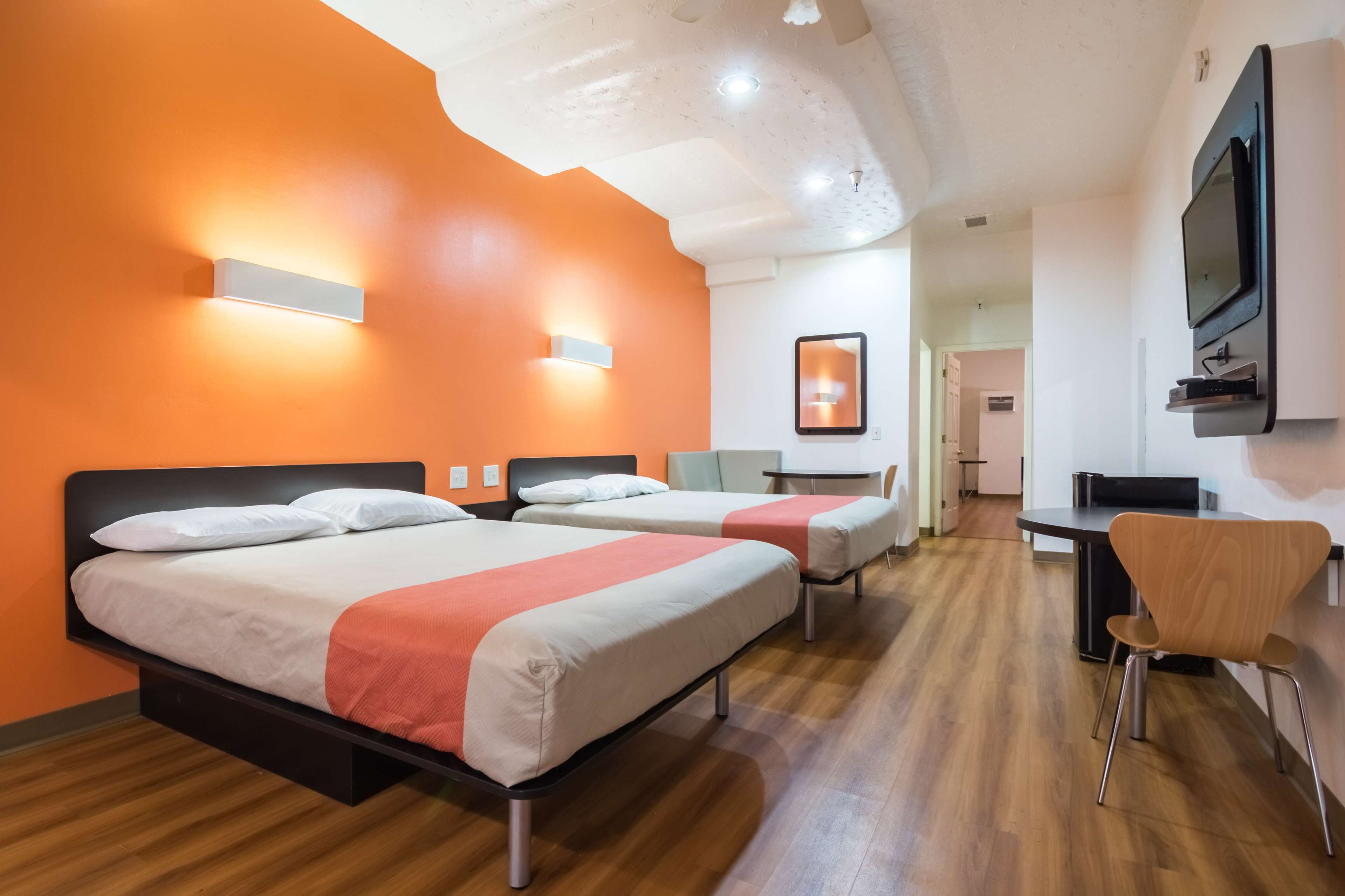 A hotel room with two beds, a desk, a chair, and a TV mounted on the wall.