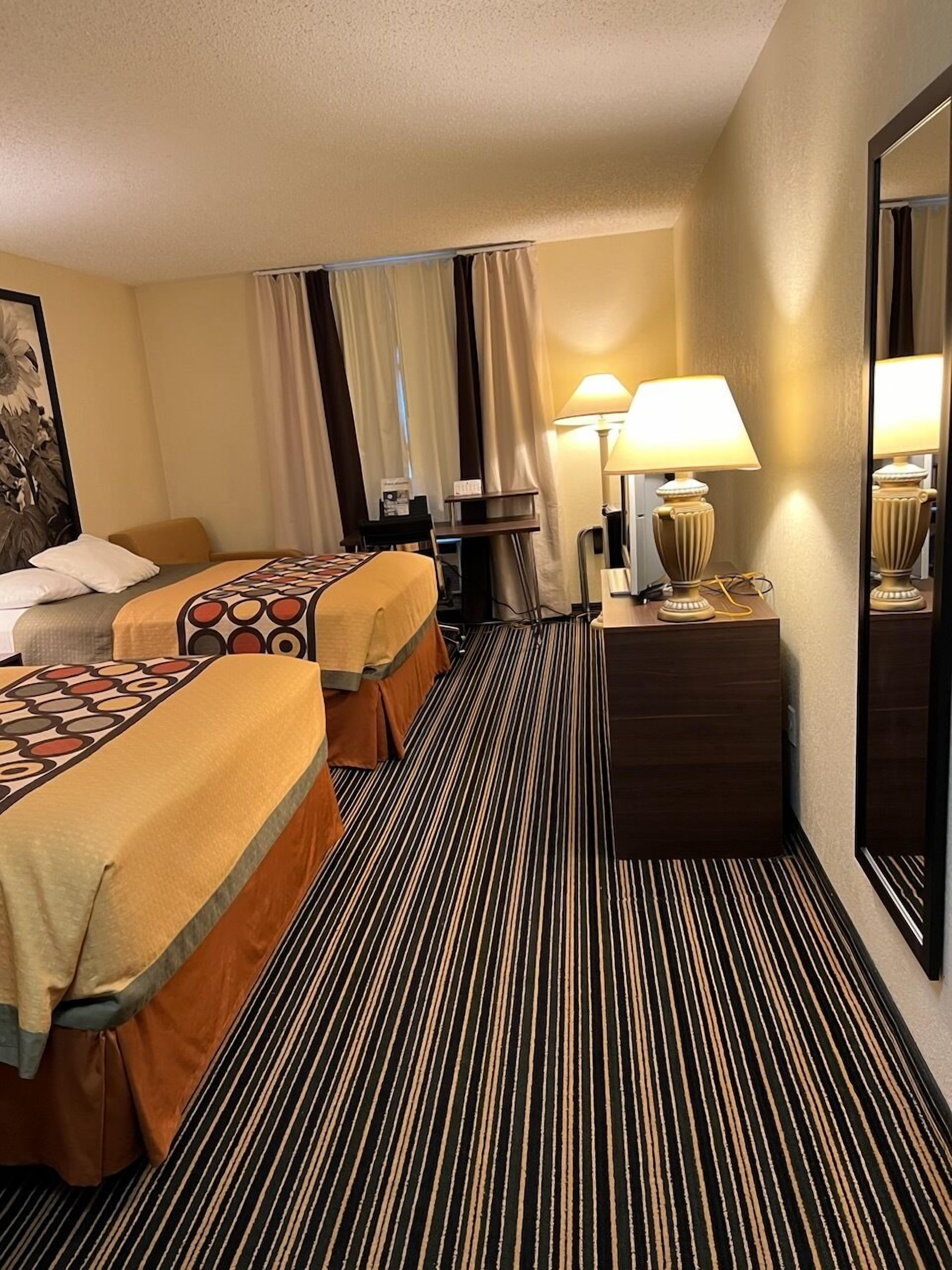 A hotel room with two beds, a desk, a lamp, and a mirror.