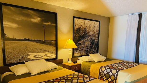 A hotel room with two beds, a nightstand, a lamp, and two large framed pictures on the walls. - Super 8 by Wyndham Dodge City (Dodge City)