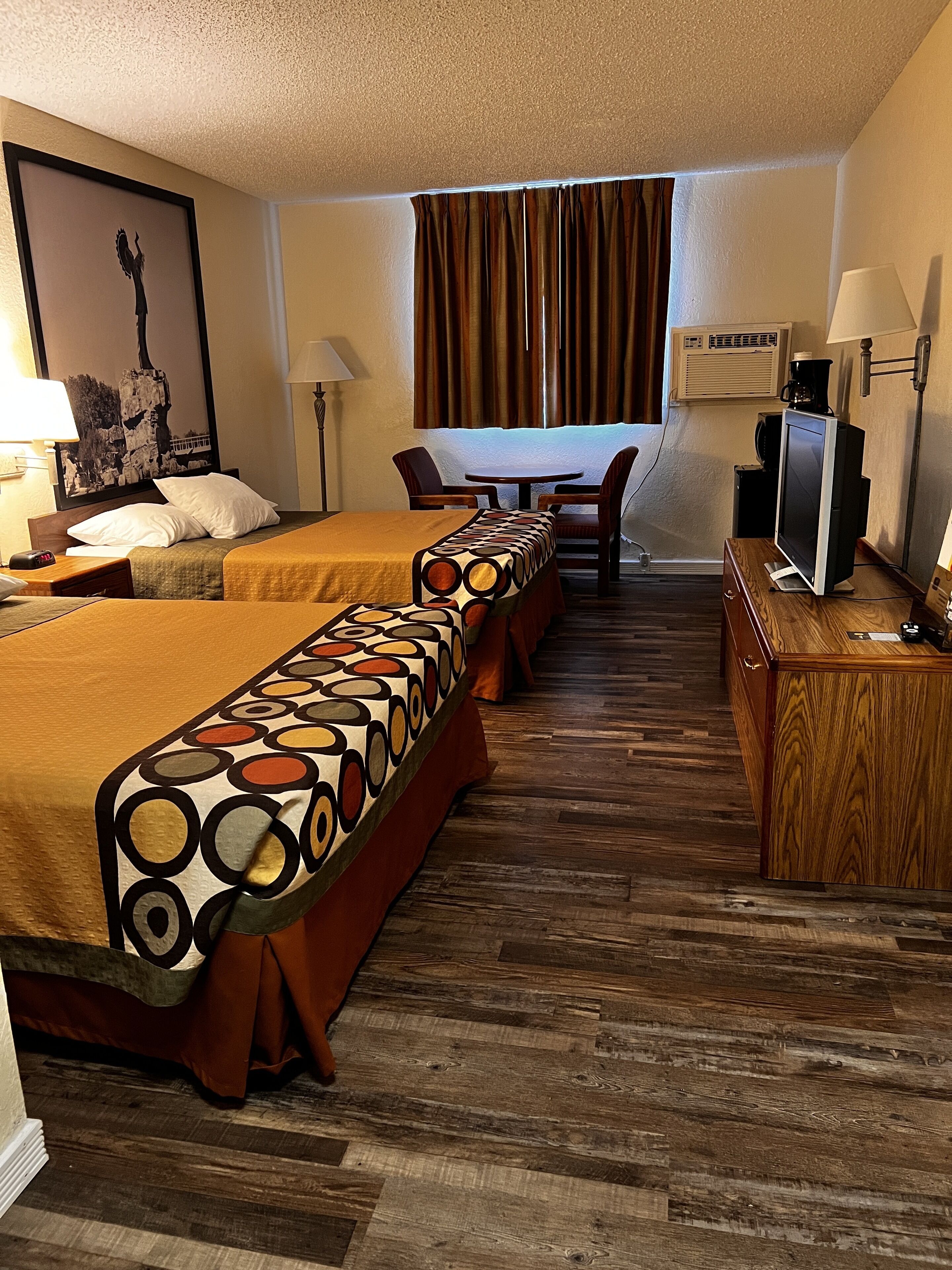 A hotel room with two beds, a desk with a computer, a chair, a TV, and a window with curtains.
