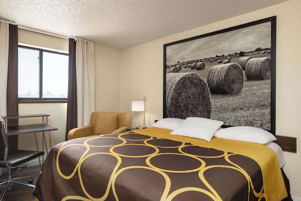 Habitación de hotel con cama, escritorio, silla y un cuadro grande con fardos de heno en la pared.