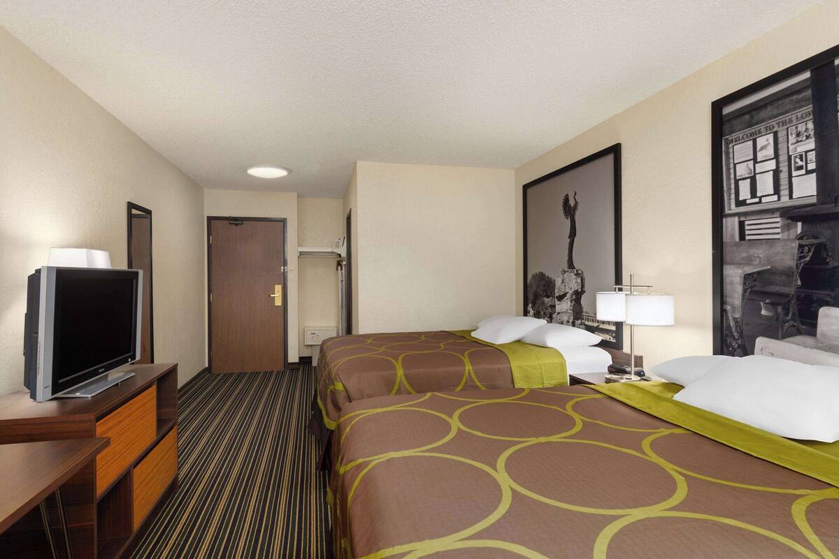 A hotel room with a television on a wooden stand, a bed with a patterned bedspread, and a framed picture on the wall.